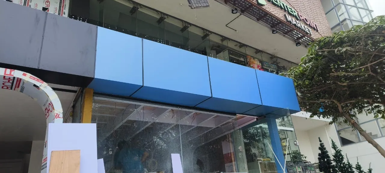 Blue ACP panel signage fascia board being installed on a commercial shop front near Center Point Market in Bangalore