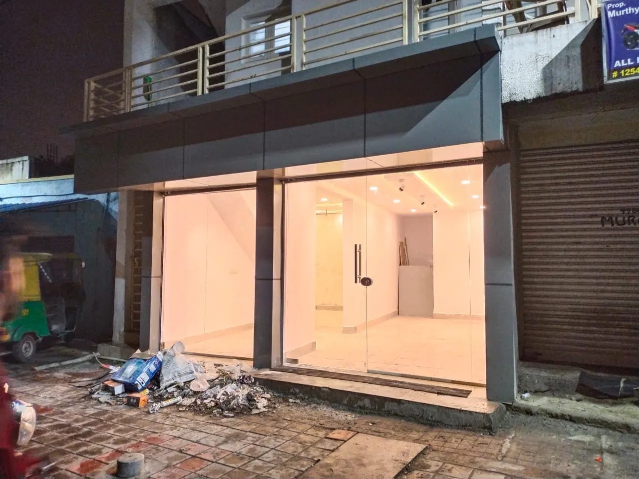 Completed grey ACP cladding shop front with frameless glass door and warm interior lighting at night in Bangalore