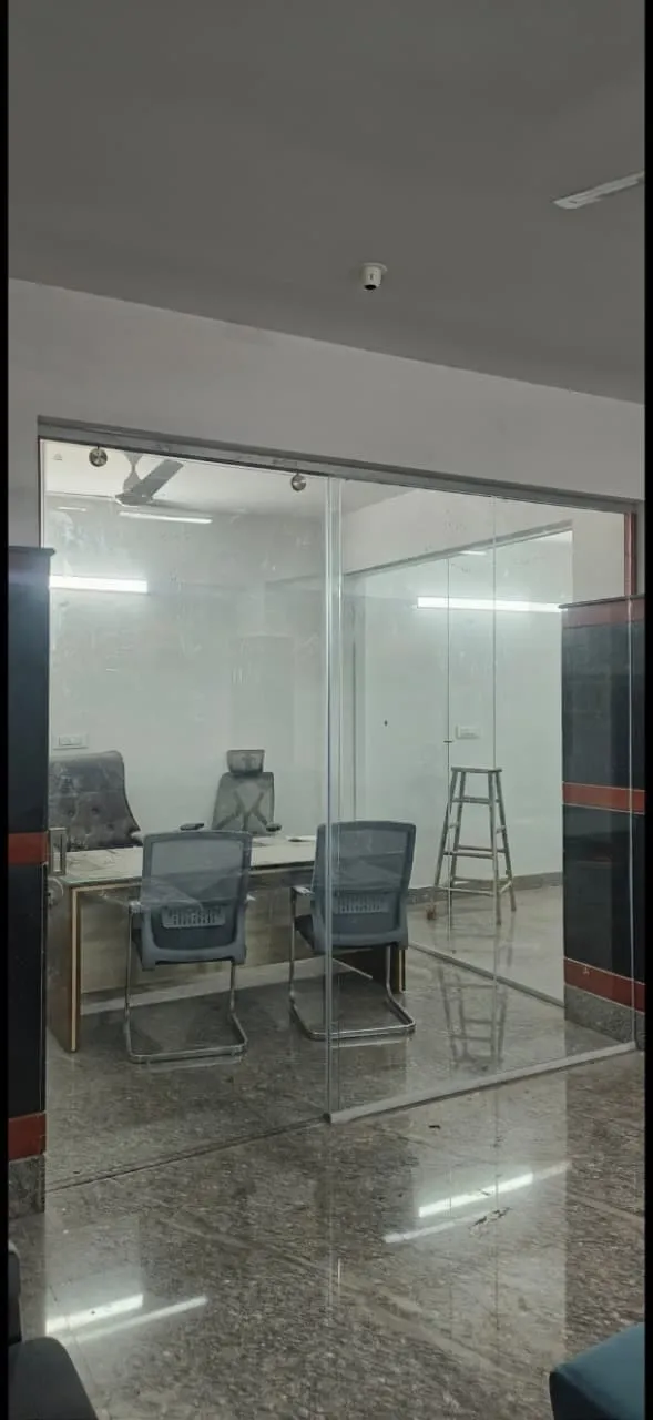 Frameless toughened glass office cabin partition enclosing a meeting room with chairs and desk inside a corporate office in Bangalore