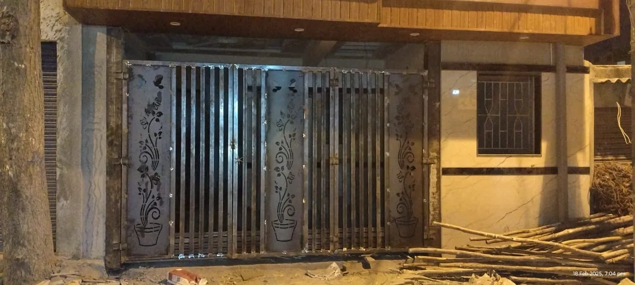 Mild steel sliding gate with CNC laser cut floral pot design and vertical bar pattern installed at a residential property at night in Bangalore
