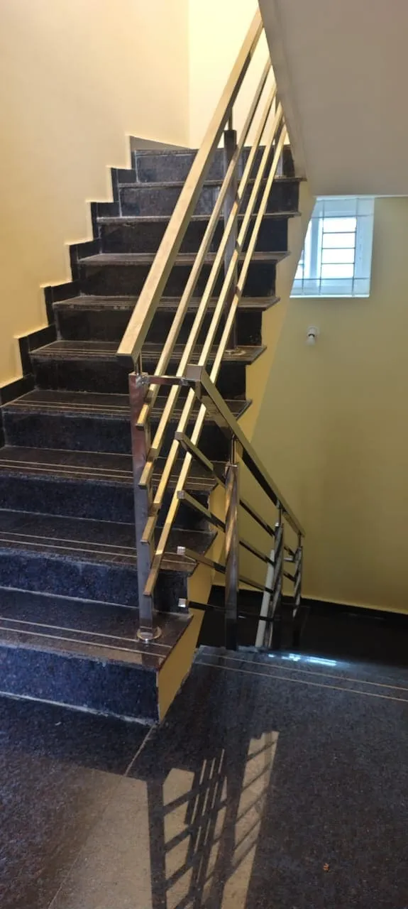 Installed stainless steel horizontal bar staircase railing on dark granite steps inside a residential building stairwell in Bangalore